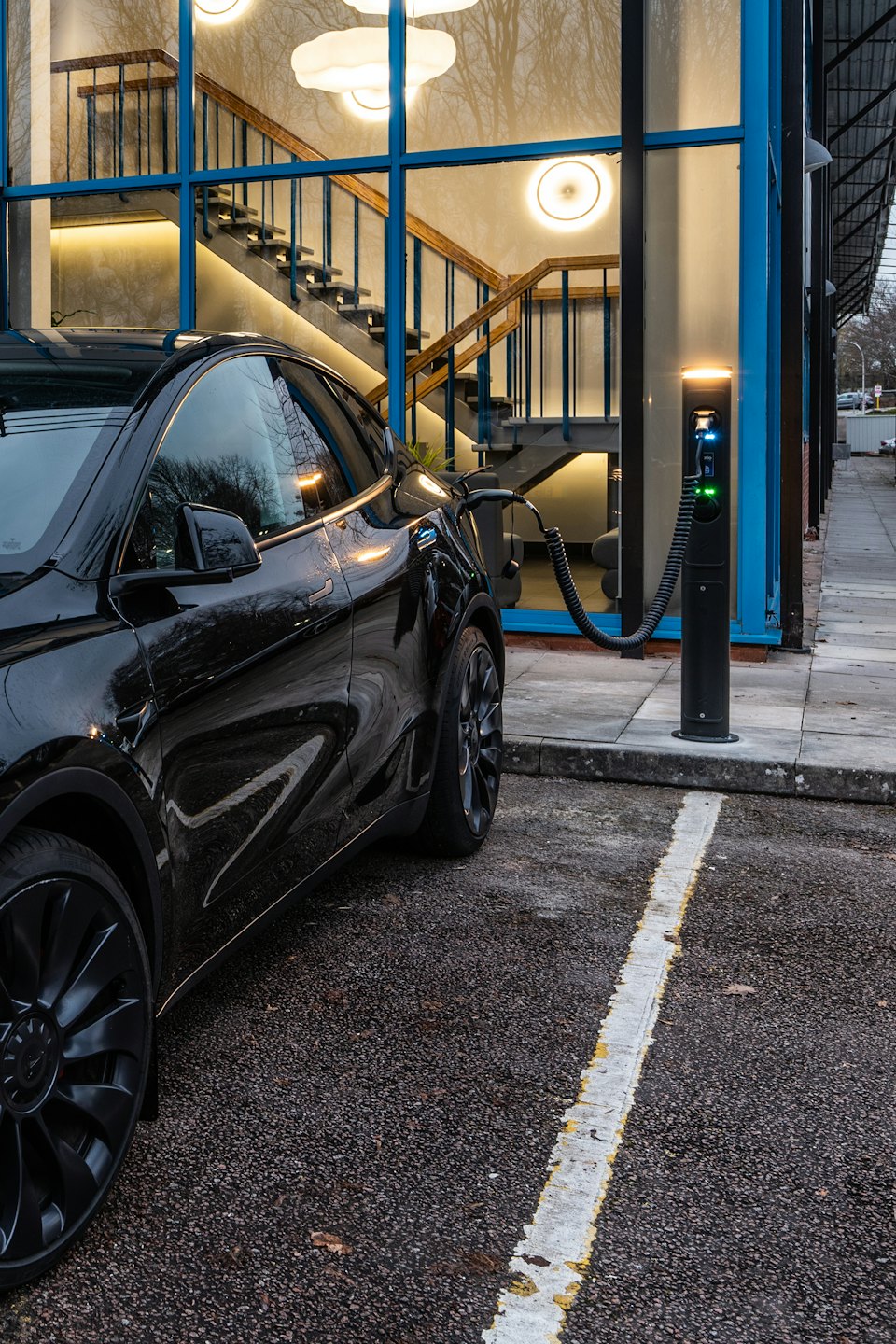 An electric vehicle charging outside a modern building with glass windows.