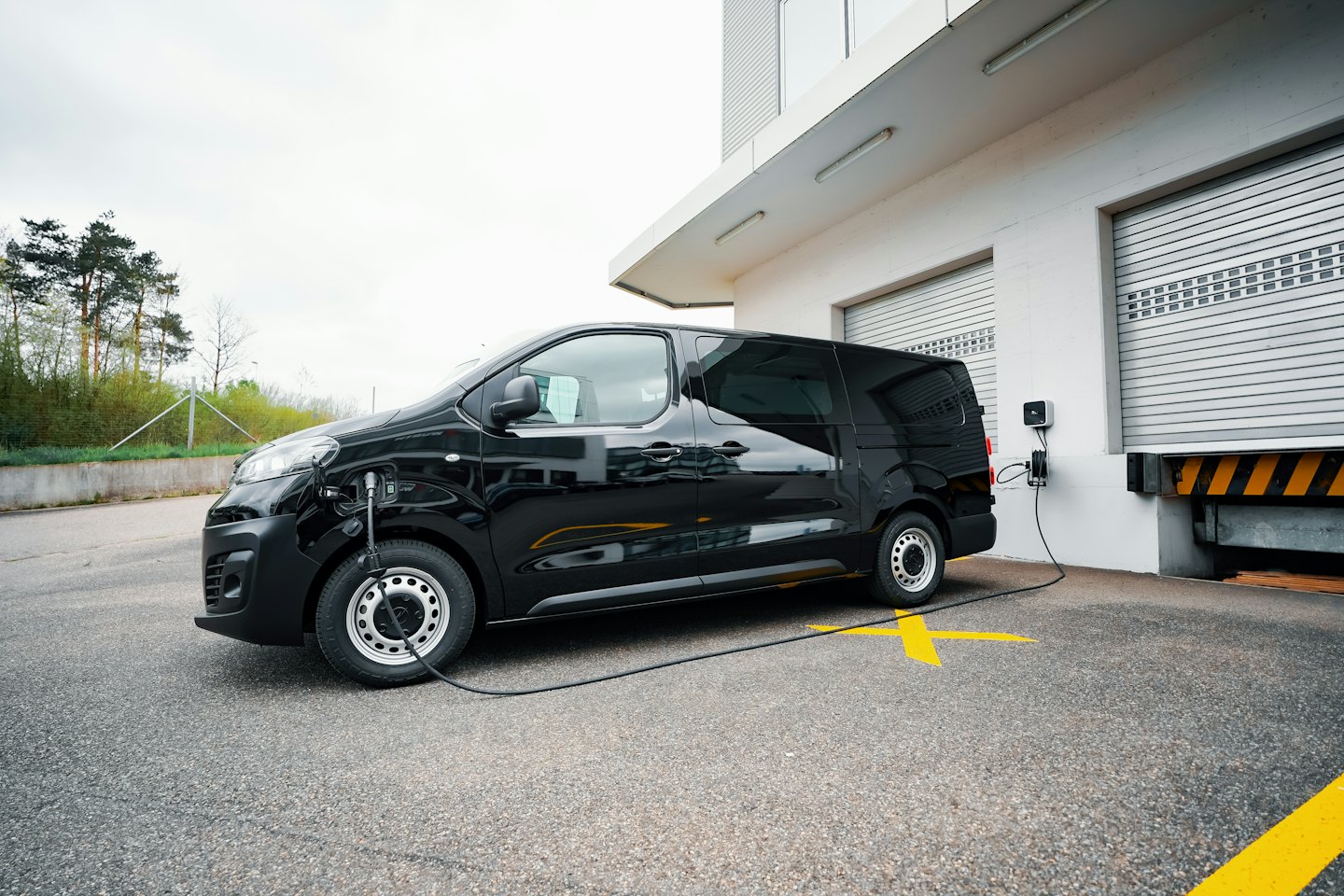 Black electric van charging at a modern industrial building.
